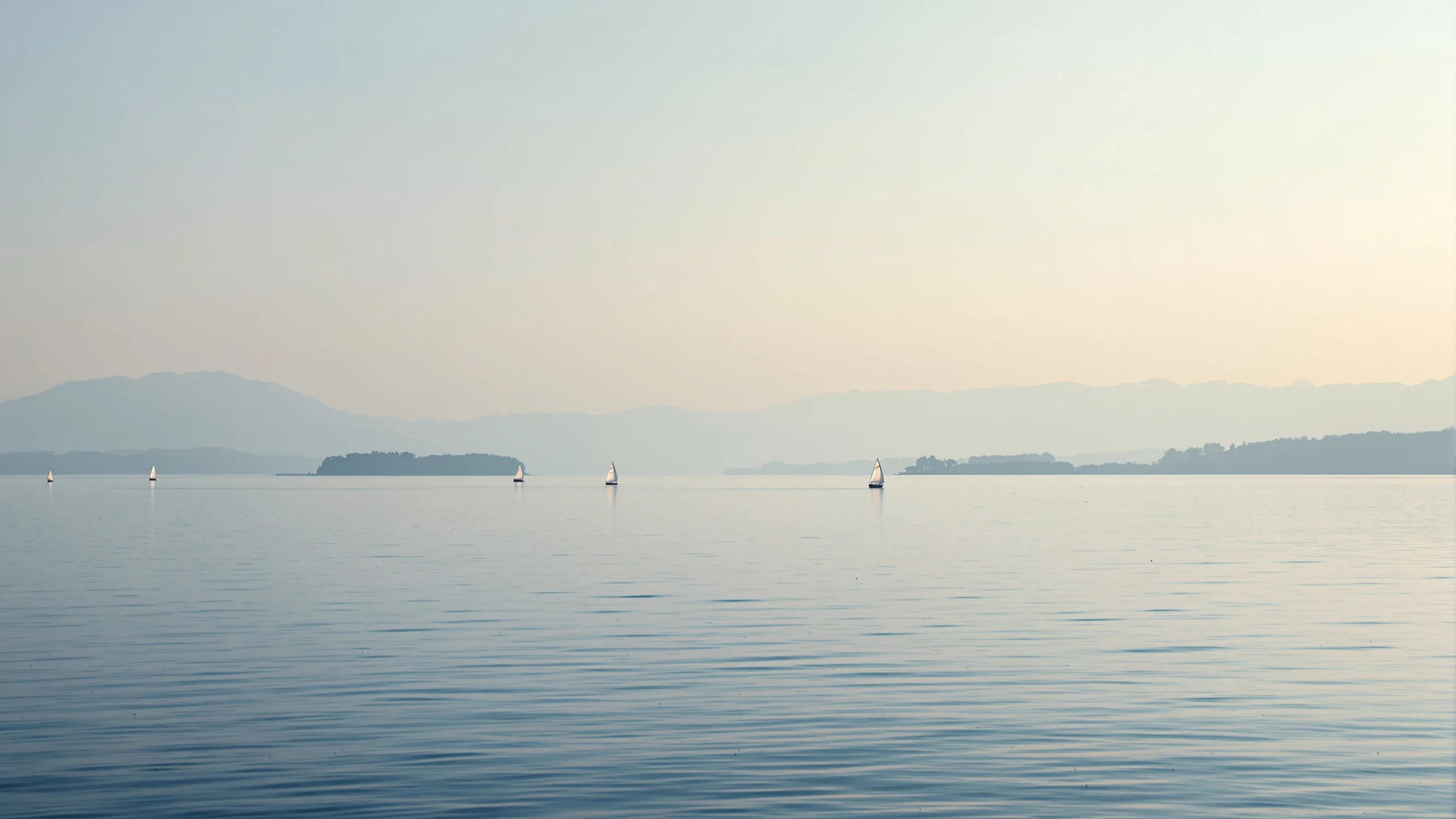 Weite Seefläche mit mehreren kleinen Segelbooten weit auseinander im Abenddunst