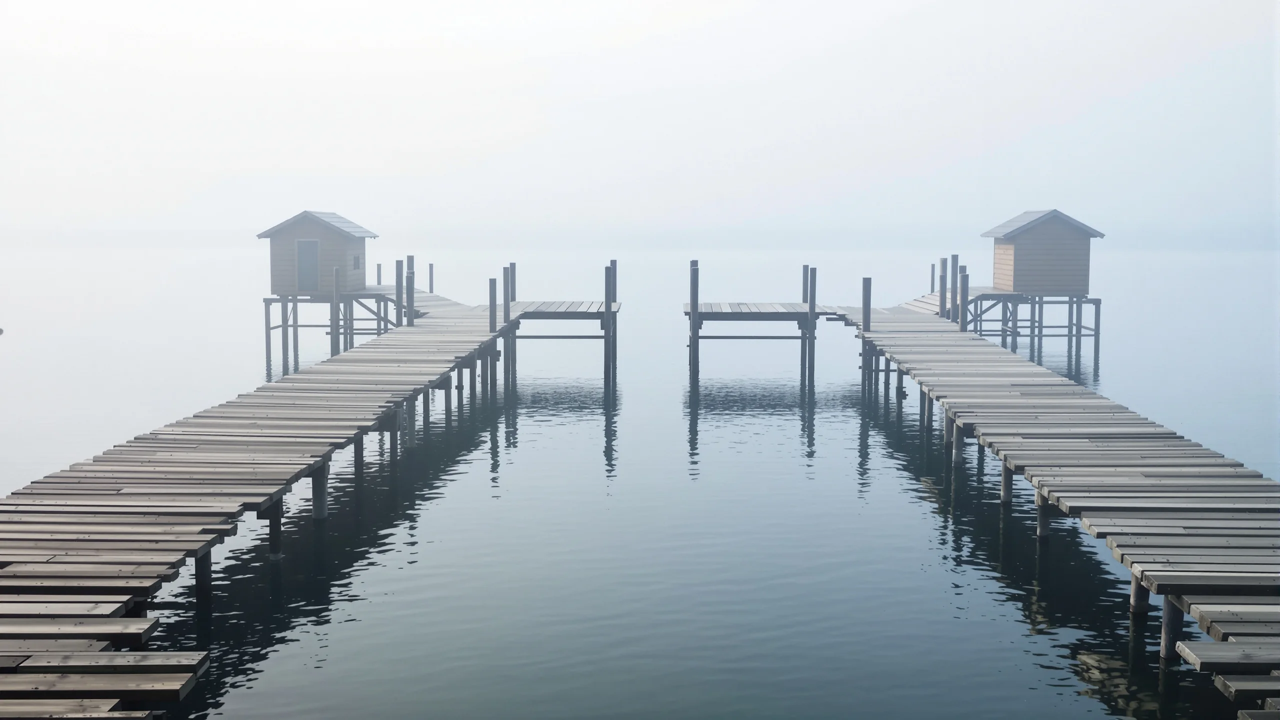 Hölzerne Stege mit zwei kleinen Badehäusern über völlig stillem Wasser im dichten Morgennebel