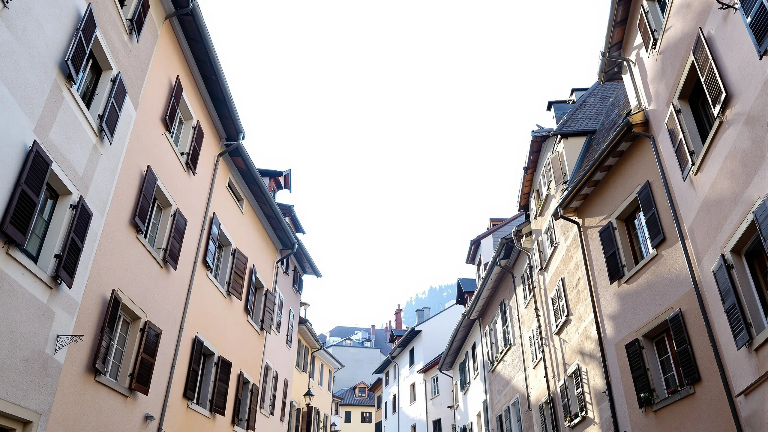 Obergeschosse einer schmalen Schweizer Altstadtgasse von unten gesehen, Fensterläden an Putzfassaden, Morgenlicht zwischen den Häusern