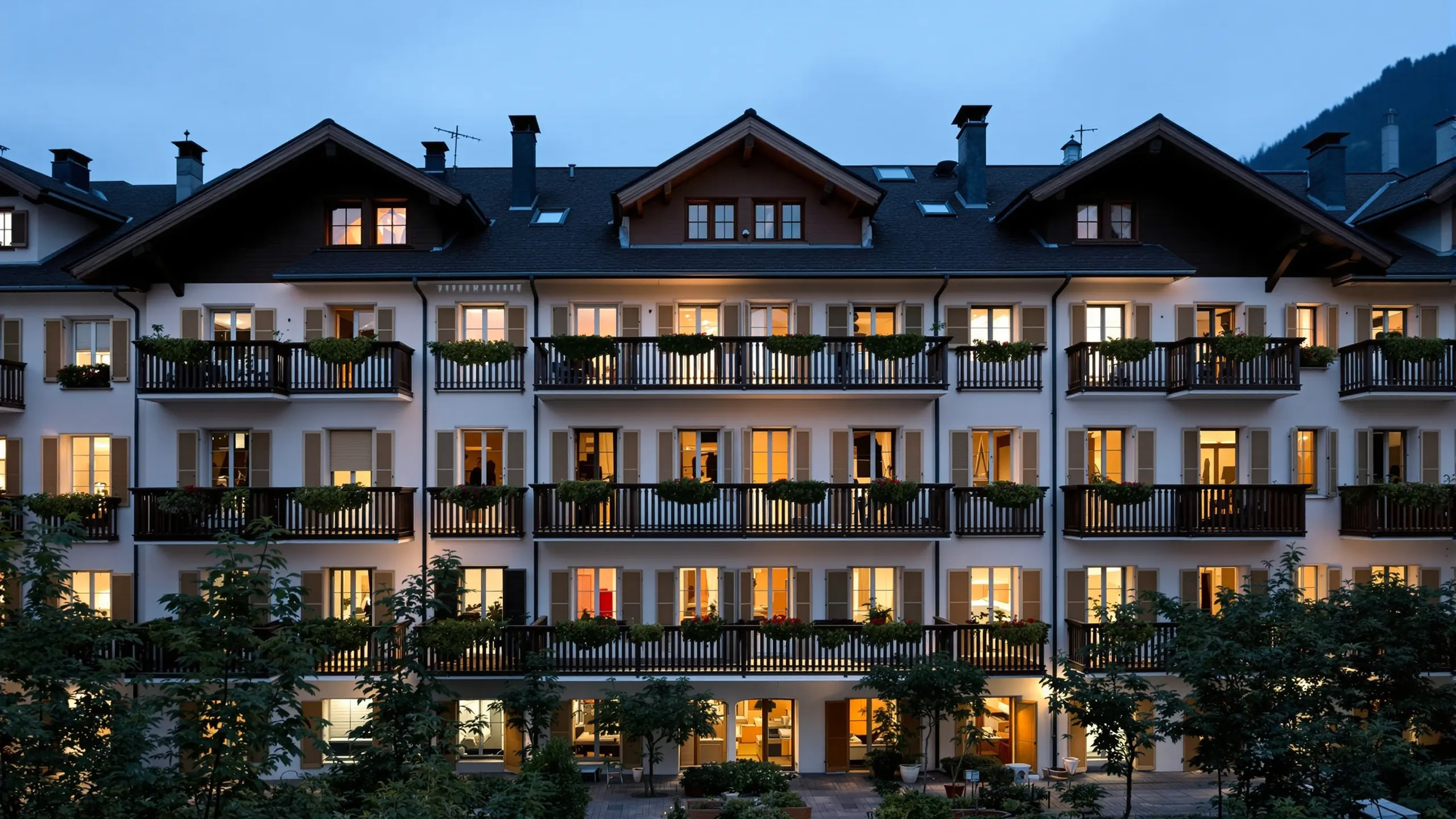 Obergeschosse Schweizer Wohnhäuser mit Fensterläden und bepflanzten Balkonen in der blauen Stunde, in fast jedem Fenster brennt Licht
